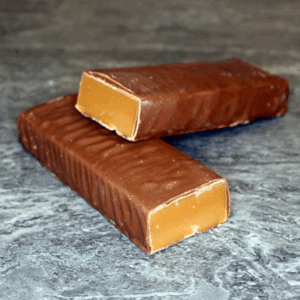 Two pieces of vanilla fudge coated in milk chocolate on a textured surface.