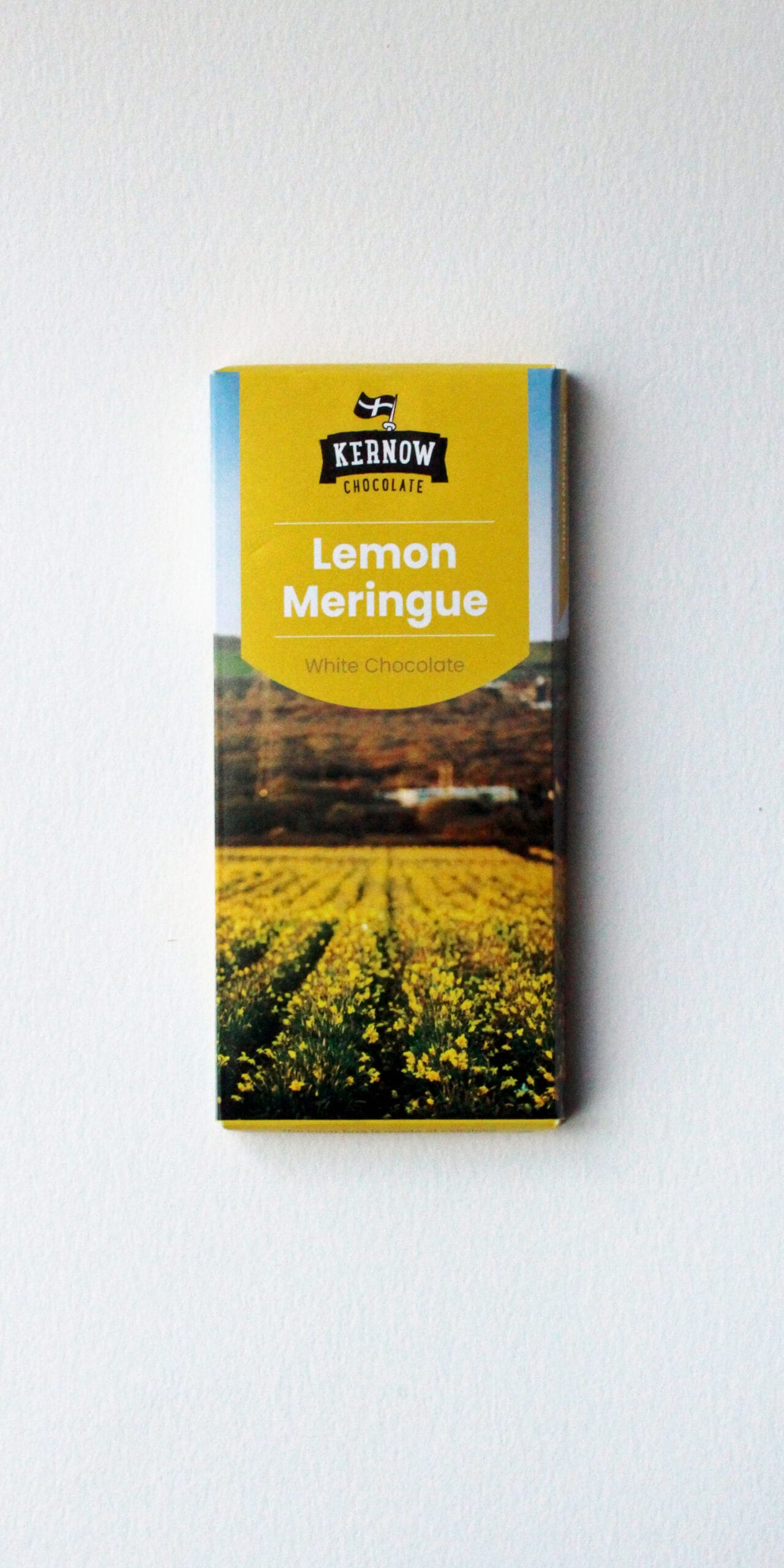 Kernow Chocolate Lemon Meringue white chocolate bar with a bright yellow label, rectangular packaging, and a countryside field image on its lower half.