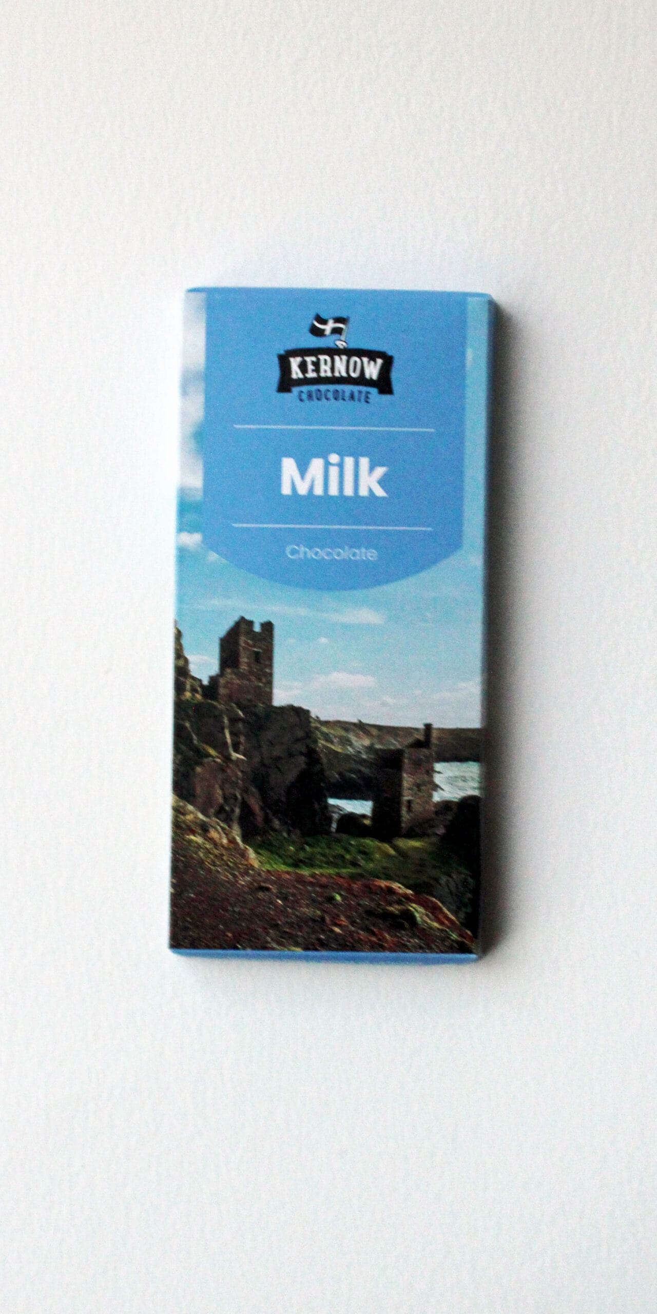 Milk chocolate bar by Kernow Chocolate in blue packaging featuring a coastal landscape with rocks and sea, set on a white background for display on a product page