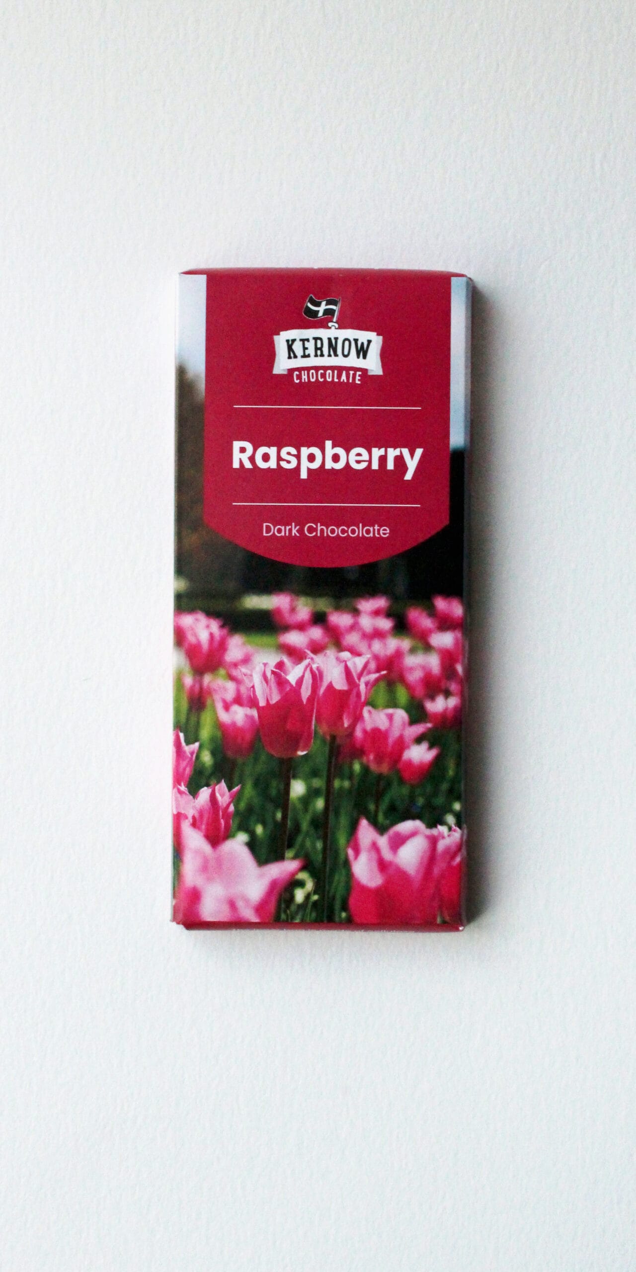 Kernow Chocolate Raspberry Dark Chocolate bar with a red label and a field of pink tulips on the lower portion, set against a white background